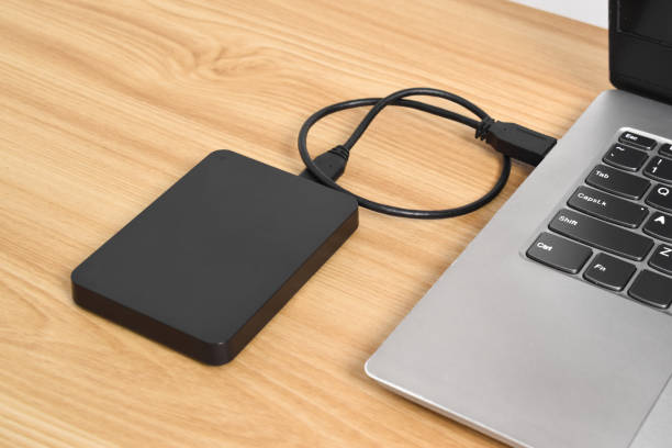 istock External backup hard disk drive connected to laptop on wooden table 2153405171