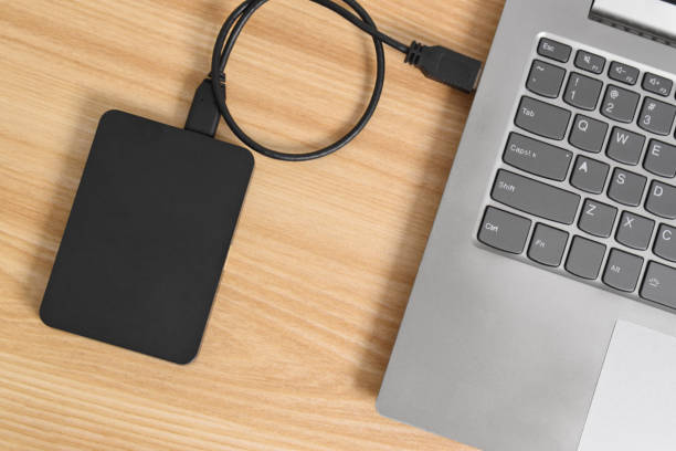 istock External backup hard disk drive connected to laptop on wooden table 2153405201