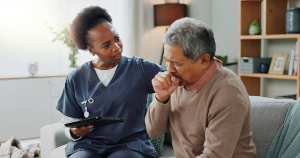 istock Home, nurse and senior man with cough or tablet in consultation with support or help. Sick, patient or elderly caregiver with person in hospice with lung cancer, tuberculosis or breathing with asma 2153405368