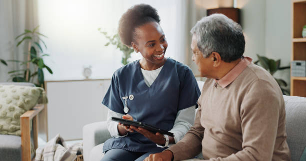tablet, healthcare and african nurse in home with senior man, internet and online help on sofa. young caregiver, elderly person and technology for learning or telehealth and care in chronic illness - ouderenzorg stockfoto's en -beelden
