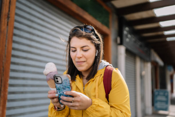 istock A woman in a yellow jacket is looking at her cell phone while holding an ice cre 2153405590
