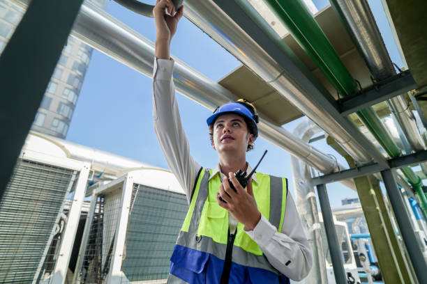 istock Industrial engineer adjusting pipeline valve with radio communication on construction site. Engineer on urban construction site using radio to coordinate with team on a sunny industrial rooftop. 2153406477