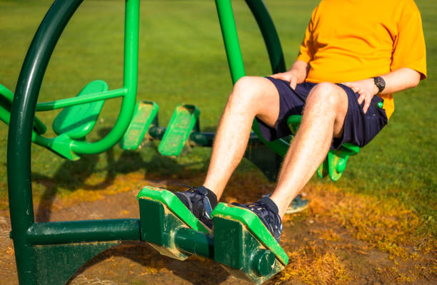 A mid adult male in his 30s uses the leg press at an outdoors gym in the park.