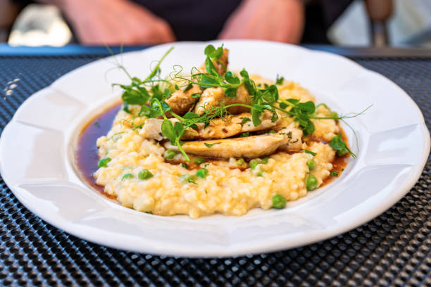 Italian risotto with chicken breast,pea and sprouted pea on white plate on table, part of hand.