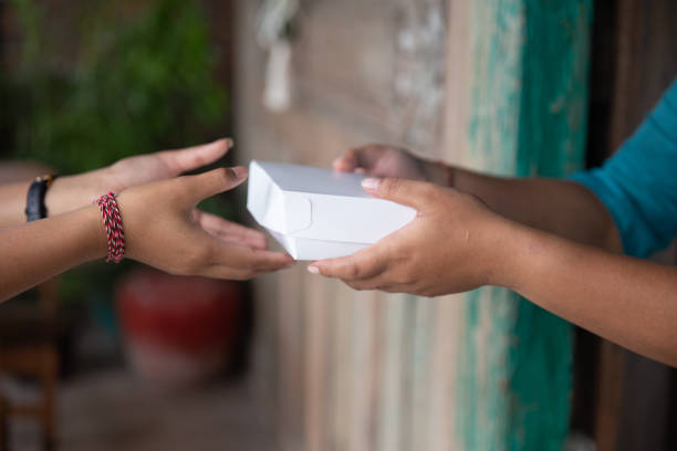 Close-up shot of Unrecognizable Hand Giving a Take-Out Food Order to customer. concept : take-out food, paper box packaging, food delivery, takeaway order, unrecognizable hand, eco-friendly packaging, food service, restaurant takeout, to-go food, sustainable food packaging