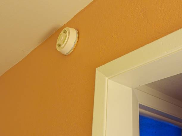Smoke detector hanging on brightly painted wall with cool outdoor light from adjoining room. Contrasts in color in vintage hotel room, with copy space.