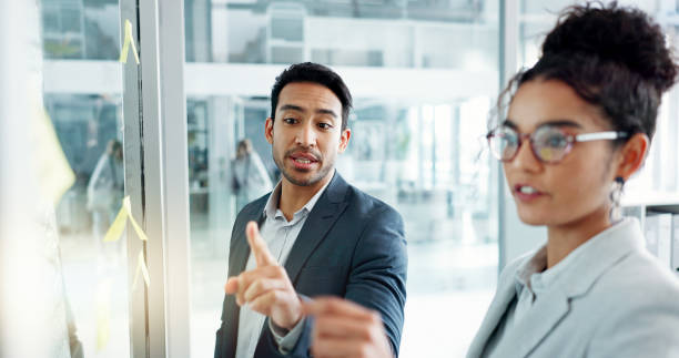 istock Business man, woman and planning by glass board, point and talk with thinking, notes and problem solving. Corporate partnership, brainstorming and discussion with moodboard, decision and solution 2153423592