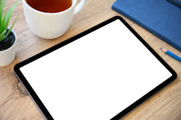 Tablet with isolated screen on wooden table with blue notepad in office