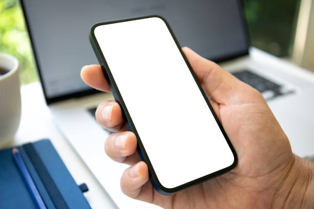 istock Male hand holding phone with isolated screen on laptop background 2153426723