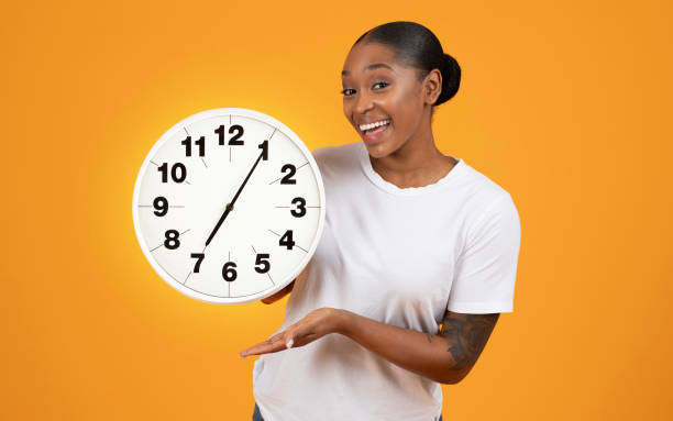 istock Smiling African American lady holds big clock over orange backdrop 2153440915