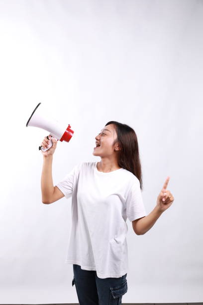 istock Happy beautiful Asian woman talking on megaphone to sideways while pointing other side. isolated on white background 2153448256