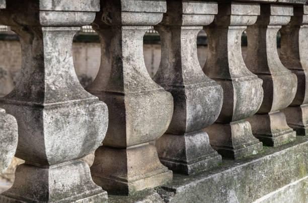 The image displays a row of metal fence posts, which are dark blue or black in color. Each post is topped with an ornate, gold-colored decorative finial. The finials have an intricate, ornamental design, resembling a variation of a fleur-de-lis or a similar cruciform patter. These are ornamental caps designed to add a decorative and sophisticated element to a fence. They are typically made of metal, such as cast iron or stainless steel, and may be gold-plated or have a gold-tone finish to withstand outdoor elements. Regular cleaning is necessary to maintain the shine and prevent environmental pollutants from dulling the finish over time.