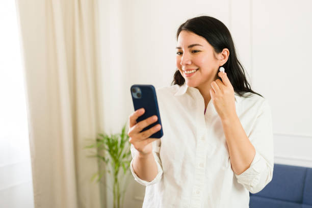 istock Happy young woman using her smartphone and getting ready to take a call using earbuds, standing in a bright and comfortable living room at home 2153466227