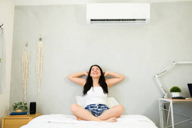 istock Young woman lounging on bed with hands behind head under a mini split air conditioner during a scorching summer day 2153468373