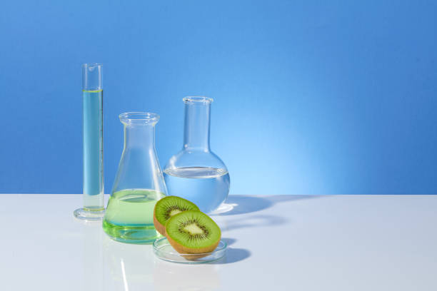 istock Frontal shot photography over blue background, measuring cylinder, boiling and erlenmeyer flask filled by transparent liquid, kiwi pieces decorated in front. Blank space for designing, copy space 2153468387