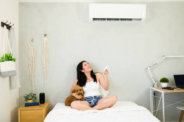 istock Happy woman using a remote control to feel the refreshing air from a mini split air conditioner on a hot summer day 2153468397