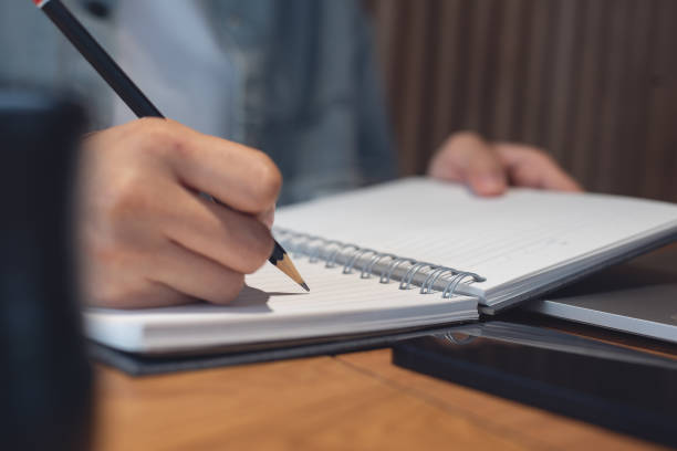 istock Business planning, E learning concept. Woman hand writing on notebook and working on laptop computer in office. Student studying online via laptop and noting on notepad, close up. 2153478761