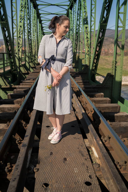 Woman walking on the deserted railway near old steel frame bridge, on a bright sunny day
