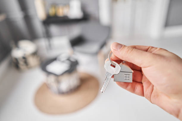 istock Men hand holding key with house shaped keychain. Modern light lobby interior. Mortgage concept. Real estate, moving home or renting property. 2153490899