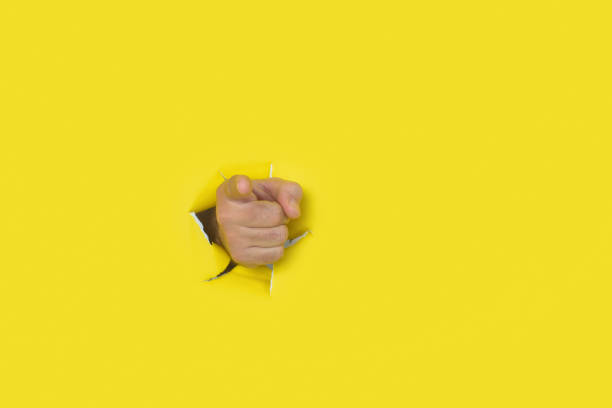 istock Male hand pointing to the front emerging from a hole in a torn paper background. 2153491182
