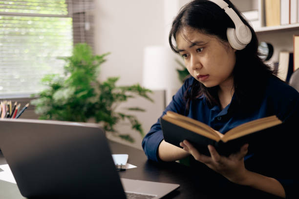 istock creative young student uses a laptop to complete online homework for college and university courses. Woman studies a book and conducts research for online academy using laptop in office. 2153493090