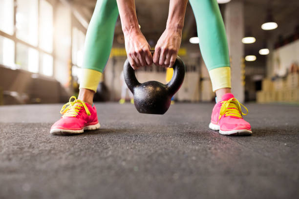 Sport woman performing kettlebell swing, holding kettlebell in hands, close up. Routine workout for woman's physical and mental health.