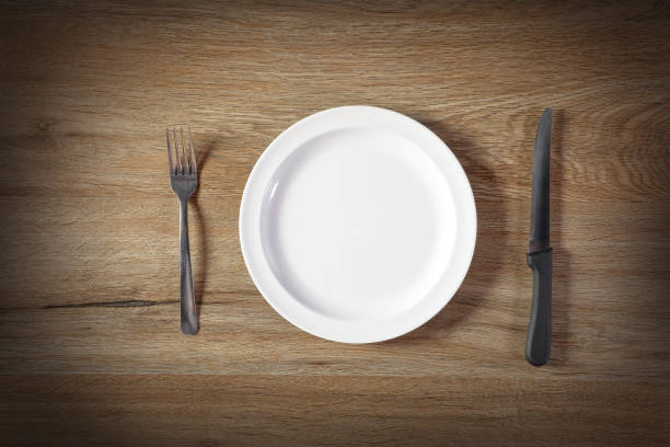 istock Empty ceramic plate with fork and knife on wooden table 2153518898