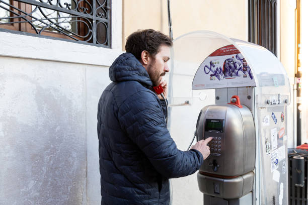 Venice, Veneto, Italy - Jan 23rd, 2024: Man using a payphone in the streets of Venice
