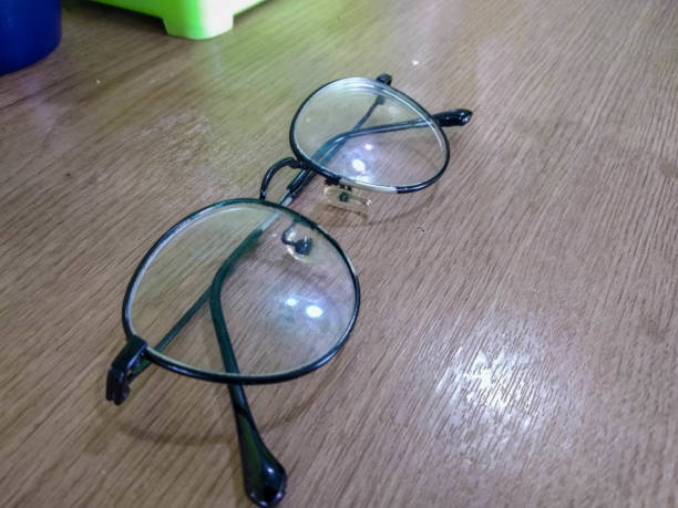 Close-up of vintage round eyeglasses with thin brown frames resting on a reflective surface, with soft bokeh lights glowing in the blurred background.