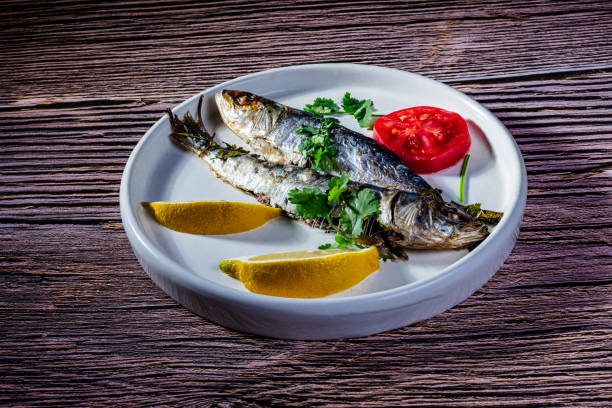 A dish with two oven-roasted sardines, accompanied with lemon, parsley and tomato.