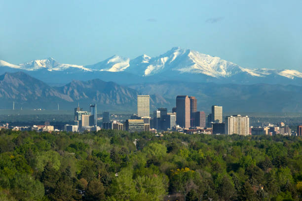 The snow covered Longs Peak and the Rocky Mountains rise over the Boulder Flatirons and Downtown Denver skyscrapers, hotels, office and apartment buildings with a golf course in the foreground.