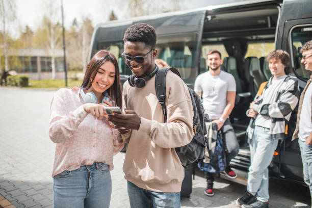 istock Smiling black man and a his female friend are watching something on a mobile phone while standing in front of the minibus, before the start of the journey 2153564936