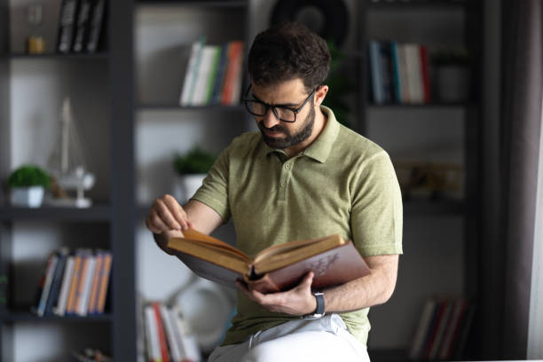 istock Young man reading book in the library 2153582527