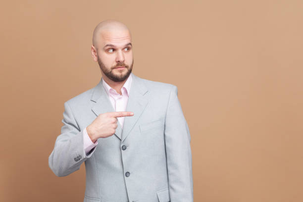 istock Serious confused bald man standing pointing at advertisement area, copy space for promotion. 2153597644