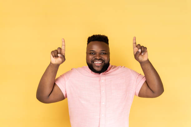 istock Man pointing up at copy space, looking smiling at camera, showing blank wall for idea presentation. 2153599016