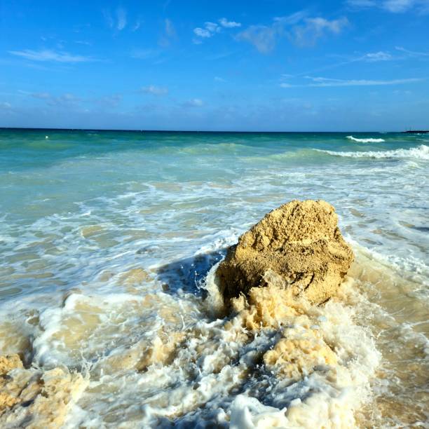 Turquoise water with waves crashing onto a rock on a beach.