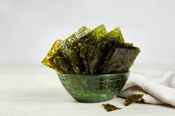 Crispy nori seaweed on green bowl on grey background. Traditional Japanese dry seaweed sheets. Crispy nori seaweed on green bowl on grey background. Traditional Japanese dry seaweed sheets. Healthy snack nori edible seaweed sheet stock pictures, royalty-free photos & images