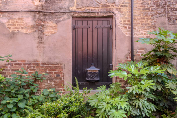 Charleston, South Carolina - May 6, 2024:  Philadelphia Alley in Charleston is a popular spot for tourists, shown here with a classic mailbox on a door surrounded by partially exposed brick wall and plants at twilight time.  HDR encoded.