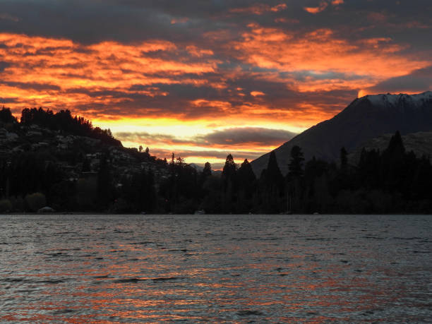 The sun rises over Queenstown and Lake Wakatipu.  On the right is The Remarkables mountain range and on the left are residential buildings of the town. This image was taken on a cold morning at sunrise on 27 April 2024.