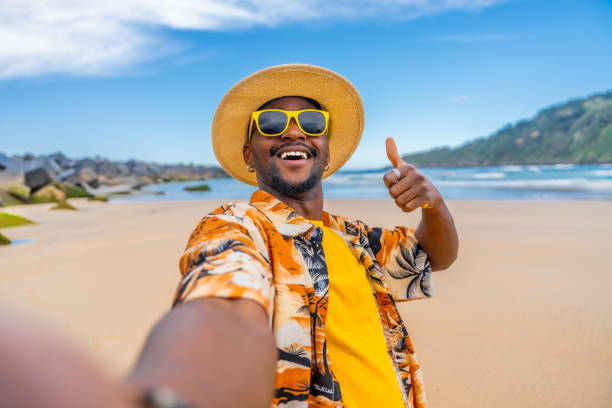 istock Man gesturing with thumb up taking a selfie at beach 2153627750