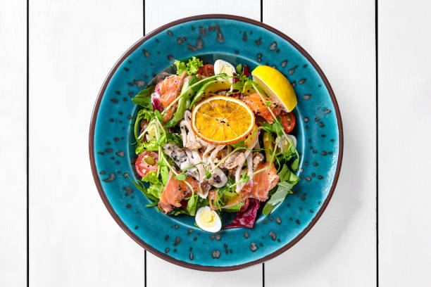 Delicious seafood salad with greens, avocado, quail egg, cherry tomatoes, squid, mussels and salted salmon seasoned with light dressing of unagi sauce garnished with fresh lemon and dried orange slice