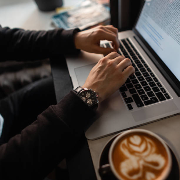 istock Man freelancer professional in black clothes with an expensive watch sits in a cafe, drinks coffee and works on a laptop 2153631517