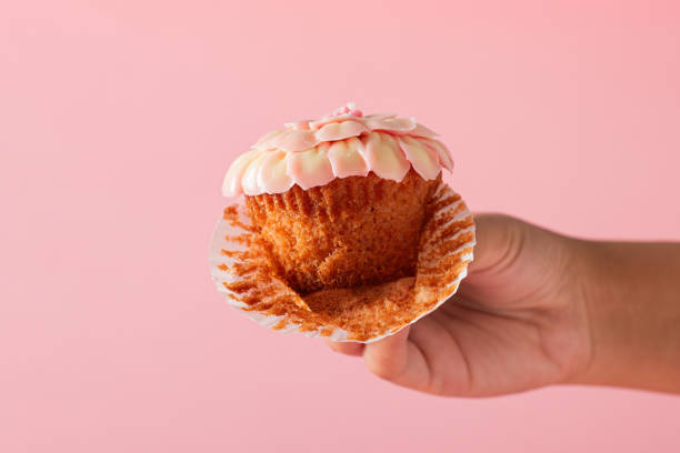 istock Female hand showing a cupcake in foreground. Pink background. 2153635558