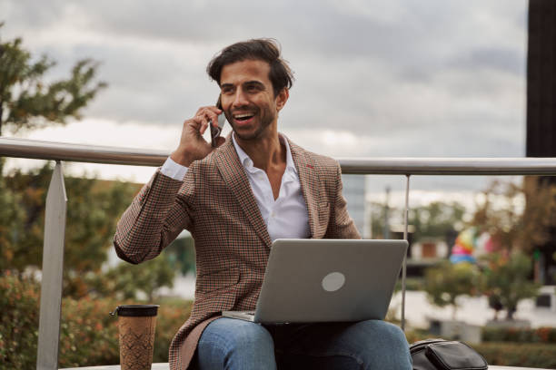 istock attractive businessman using his laptop on the street to work while talking on his smartphone 2153641801