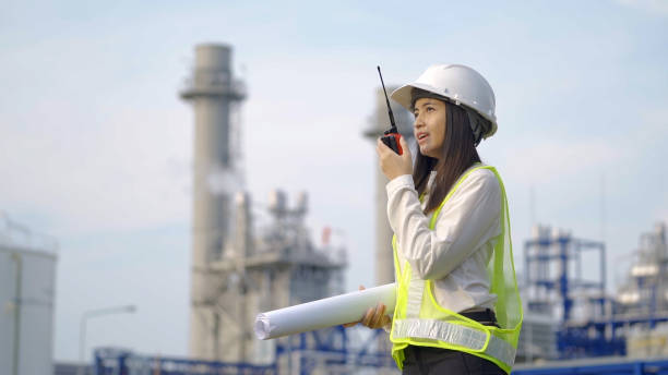 istock A female engineer in a hard hat and reflective vest holds blueprints and communicates via walkie-talkie at an industrial power plant. 2153648198