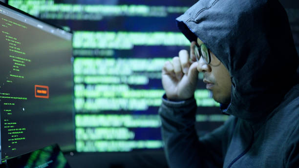 istock Hacker man in hood hacking break in to security and confidential data from victim data center by software and hacking tool in dark atmosphere hacking lab. 2153648219