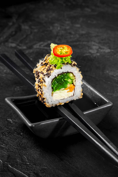 Vegetarian sushi roll on chopsticks above soy sauce