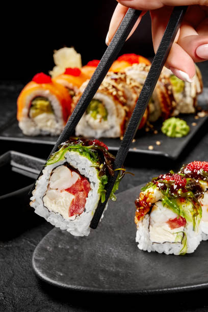 istock Female hand taking sushi roll with crab meat by chopsticks 2153652248
