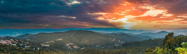 Barcelona, Spain. sunset over a mountain range with trees in foreground. Panorama clouds create a dreamy atmosphere as the sky transitions to dusk Spain Barcelona