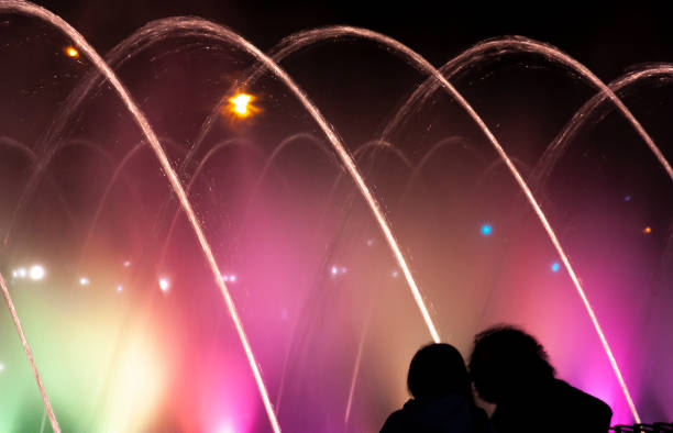 An unknown couple taking a walk around the water light fountain in Providencia neighborhood at night, Santiago de Chile, Chile, Latin America.